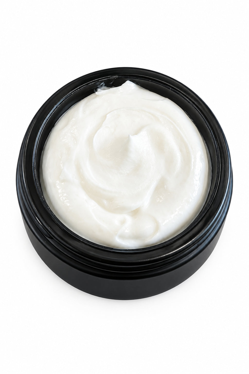 A close-up of a white cream or lotion swirled inside a round black jar, placed on a wooden tabletop with a book partially visible in the background.